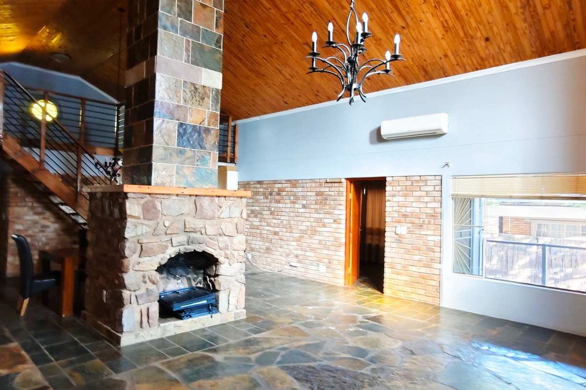 Spacious living area featuring a prominent stone fireplace, vaulted timber ceiling, slate flooring, and an open staircase leading to a mezzanine level.