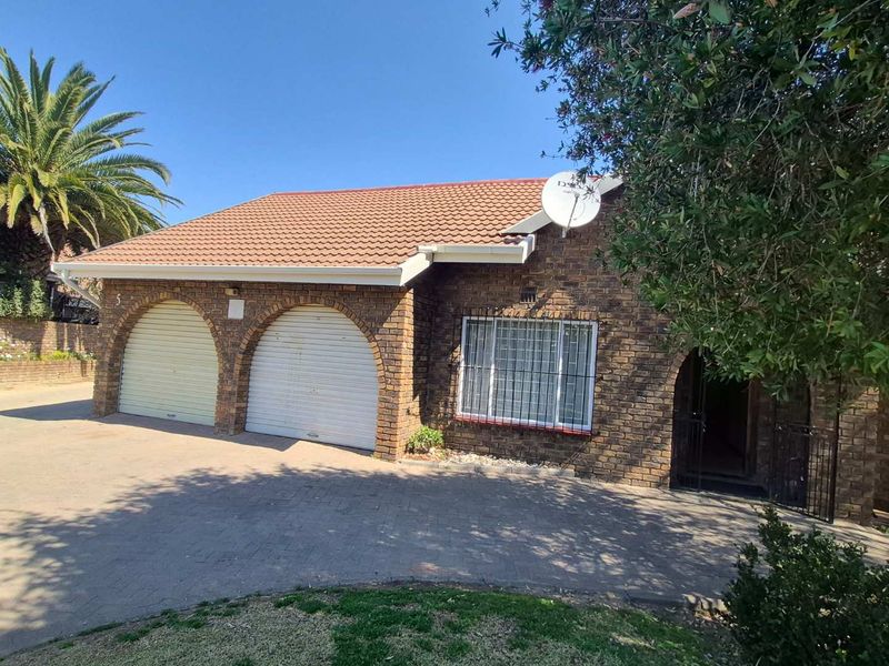 Front elevation of a brick townhouse featuring a double garage with arched openings, a tiled roof, and a paved driveway.