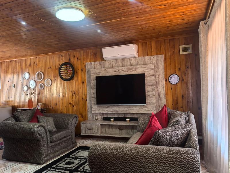 A living room featuring warm timber wall and ceiling paneling, a built-in media console, and a wall-mounted split-system air conditioner.