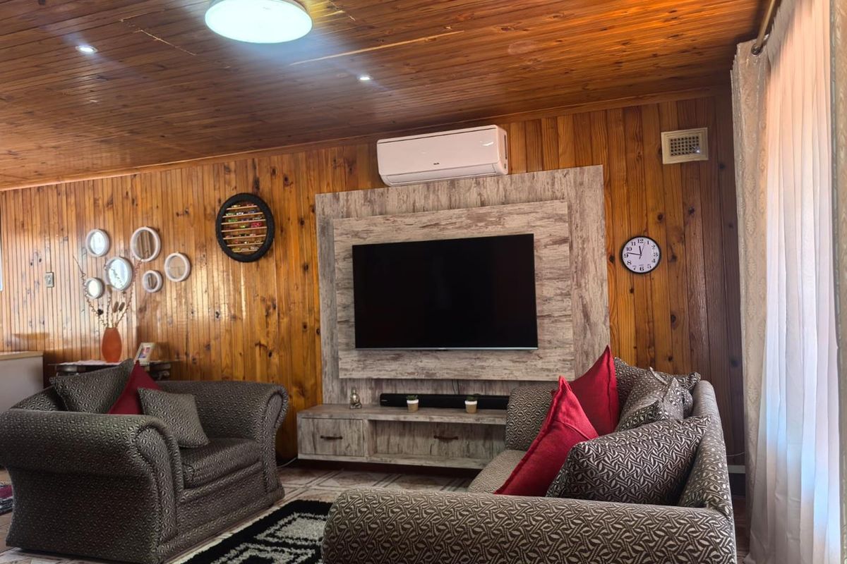 A living room featuring warm timber wall and ceiling paneling, a built-in media console, and a wall-mounted split-system air conditioner.