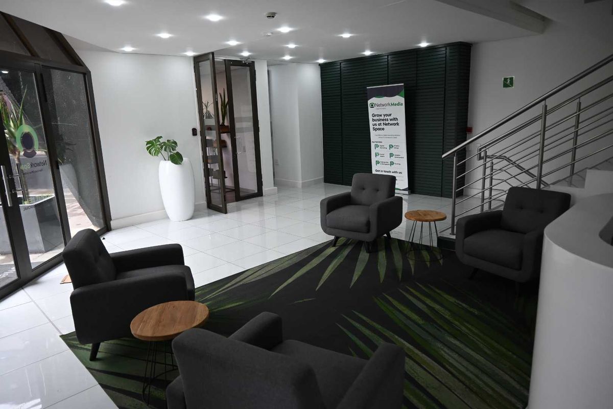 A bright and modern office building entrance lobby featuring tiled floors, recessed lighting, and a contemporary staircase with stainless steel railings.