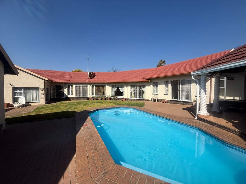 Spacious rear courtyard featuring a swimming pool, paved patio area, and a well-maintained lawn surrounded by the main house structure.