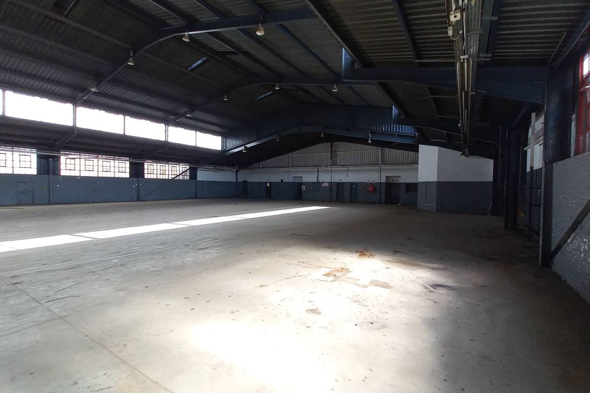 Spacious industrial warehouse featuring high ceilings, exposed steel trusses, large clerestory windows, and durable concrete flooring, suitable for various commercial or storage operations.