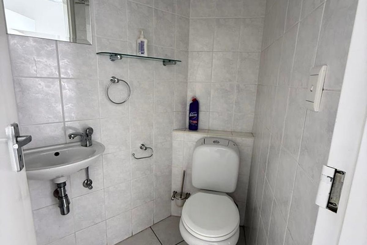 A compact guest bathroom featuring a wall-mounted basin, a standard toilet, and full-height wall tiling with a decorative border.