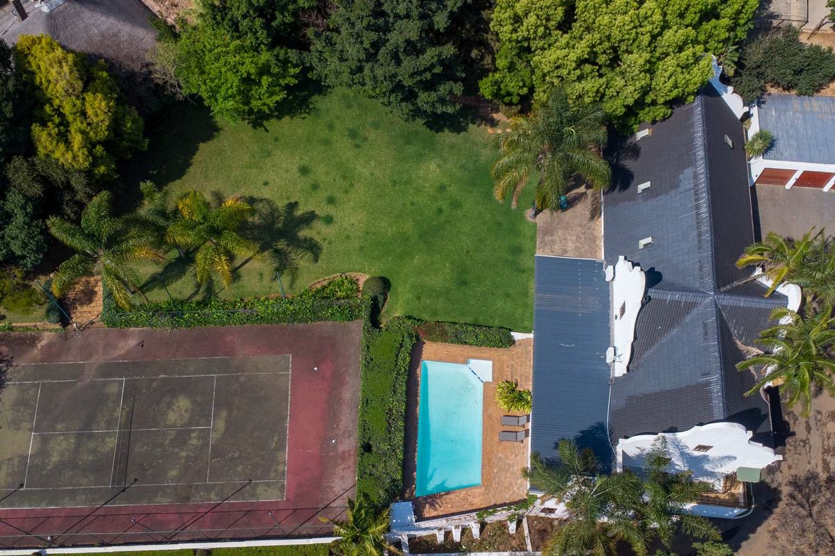Aerial view of the property featuring a large garden, swimming pool, tennis court, and main dwelling with a tiled roof and garage.