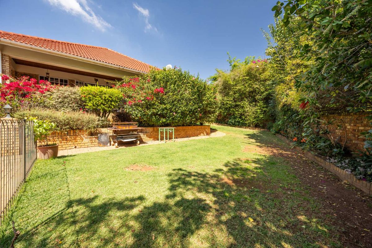 A well-maintained rear garden featuring a lawn, established landscaping, a brick retaining wall, and access to a covered patio area.