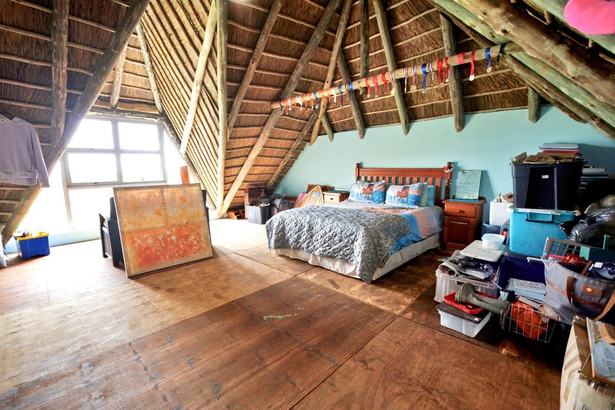 Spacious attic-style bedroom featuring a high vaulted thatched roof with exposed timber beams and large window providing natural light.