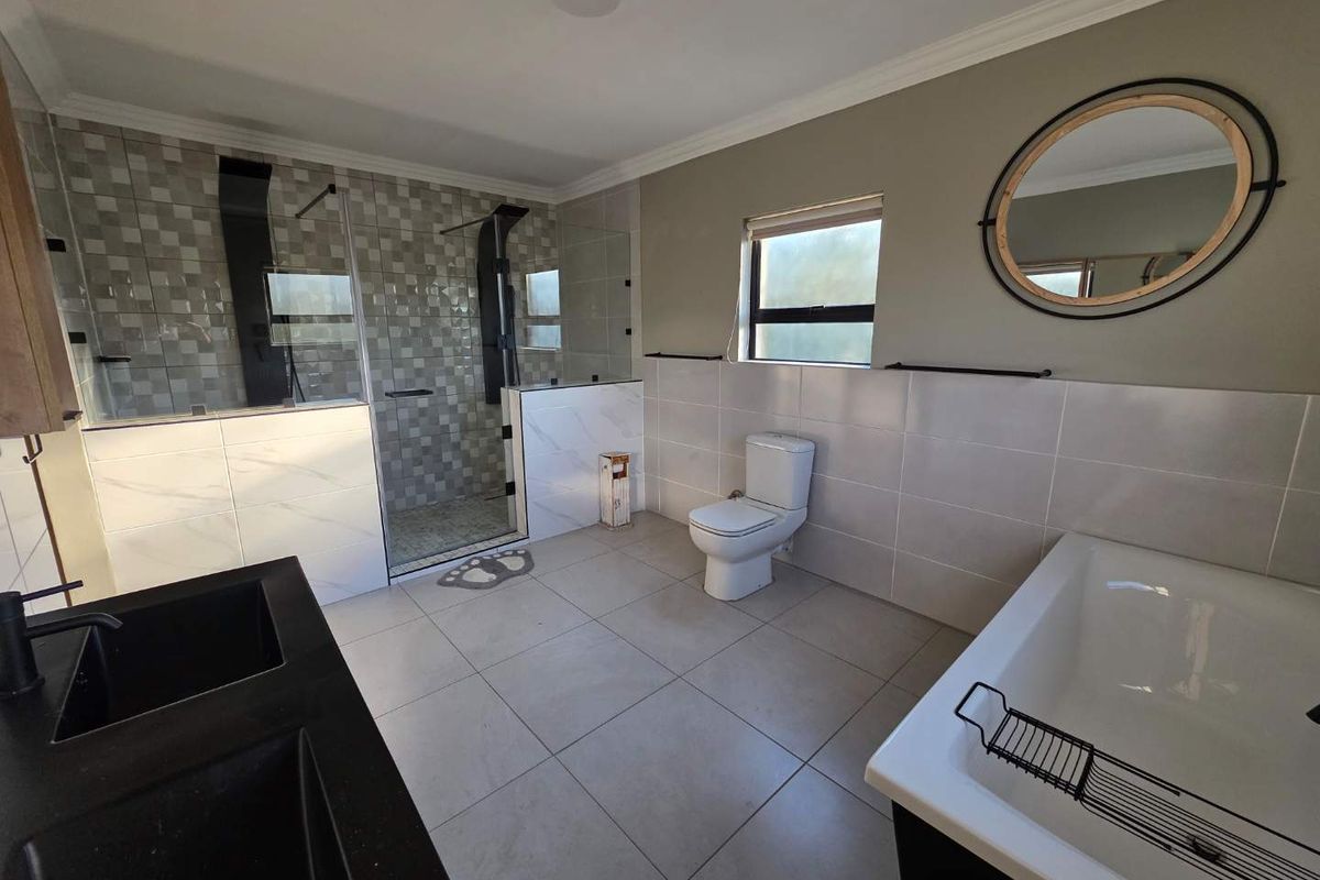 Modern bathroom featuring a walk-in glass shower, a deep soaking bathtub, dual vanity sinks, and contemporary tiled finishes.
