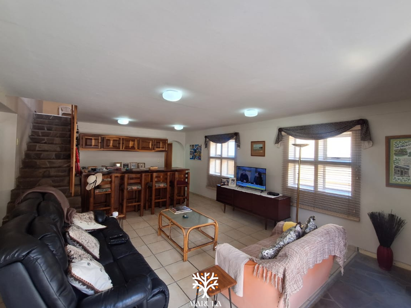 Spacious living room featuring a built-in bar area, stone staircase, and tiled flooring, offering a functional layout with ample natural light.