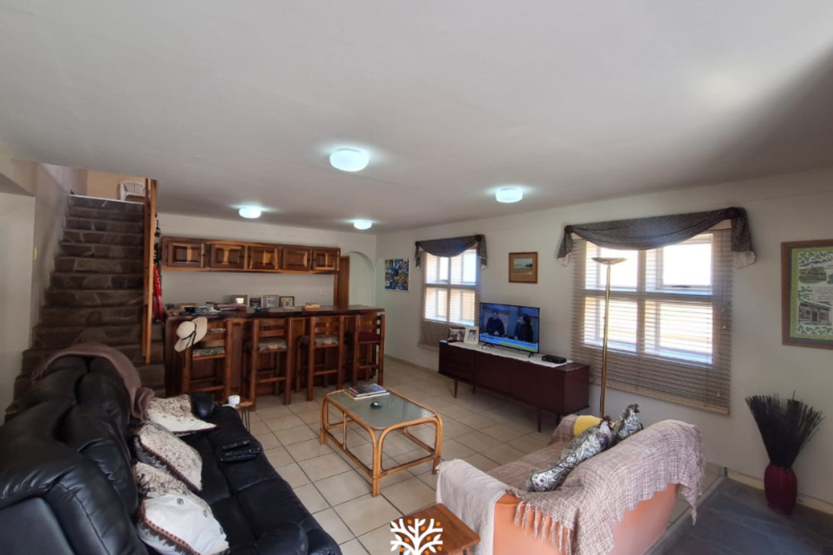 Spacious living room featuring a built-in bar area, stone staircase, and tiled flooring, offering a functional layout with ample natural light.