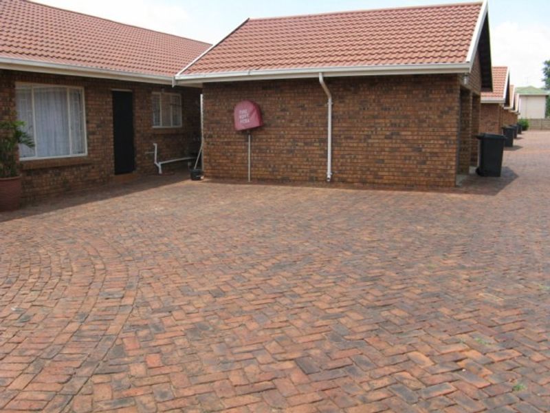 A view of the front exterior of the townhouse complex, featuring face brick construction, tiled roofing, and paved driveway area.