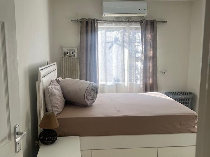 A functional bedroom featuring tiled flooring, a wall-mounted split-system air conditioner, and a central ceiling light fixture.