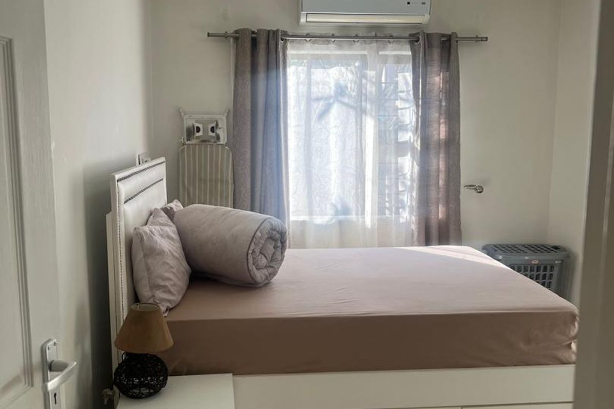 A functional bedroom featuring tiled flooring, a wall-mounted split-system air conditioner, and a central ceiling light fixture.