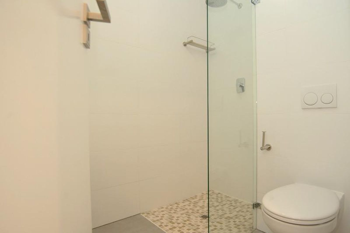 Modern bathroom featuring a wall-mounted toilet with concealed cistern and a walk-in shower with glass screen and mosaic tile flooring.