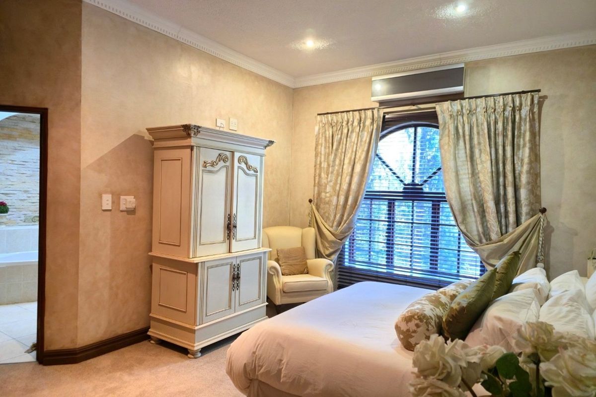 A well-maintained bedroom featuring an arched window, crown molding, and a wall-mounted air conditioning unit.