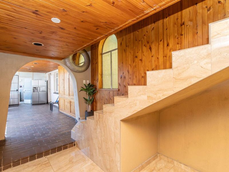 A spacious hallway featuring a stone staircase, timber-clad ceiling, and arched architectural details leading into an adjacent tiled living area.