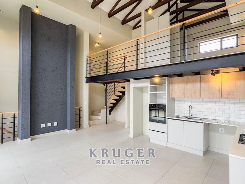 Spacious open-plan living area featuring a modern kitchen, high ceilings with exposed beams, and a mezzanine level with a metal staircase.