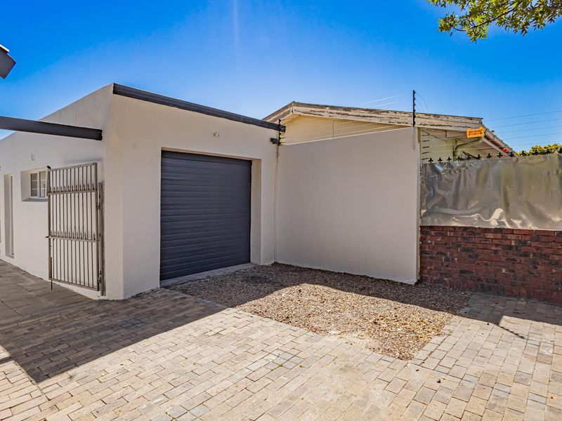 Exterior view of a single garage with a roller door, featuring a paved driveway, brick boundary wall, and integrated security fencing.
