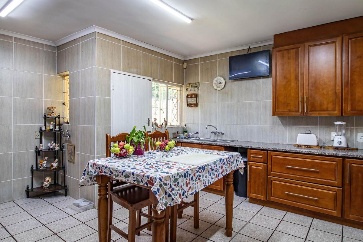 A functional kitchen featuring wooden cabinetry, granite countertops, a double sink, and fully tiled walls and floors.