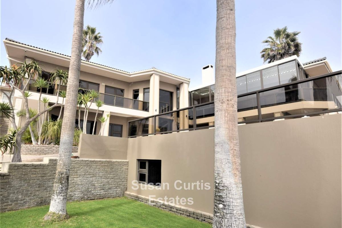 Rear exterior view of a multi-level residence featuring expansive balconies with glass balustrades, a chimney, and a landscaped garden area.