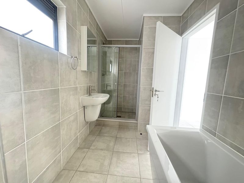 A modern, neutral-toned bathroom featuring a wall-mounted basin, a separate shower enclosure, and a bathtub with full-height wall tiling.