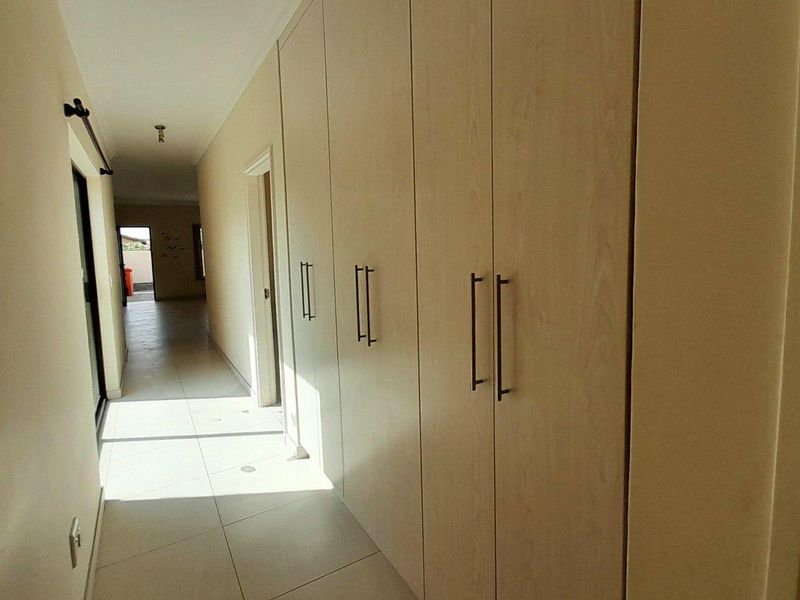 A bright, tiled hallway featuring extensive built-in storage cupboards and a sliding door leading to an outdoor area.