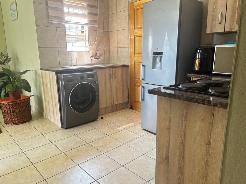 Functional kitchen featuring wood-look cabinetry, granite countertops, tiled splashbacks, and integrated space for laundry appliances.