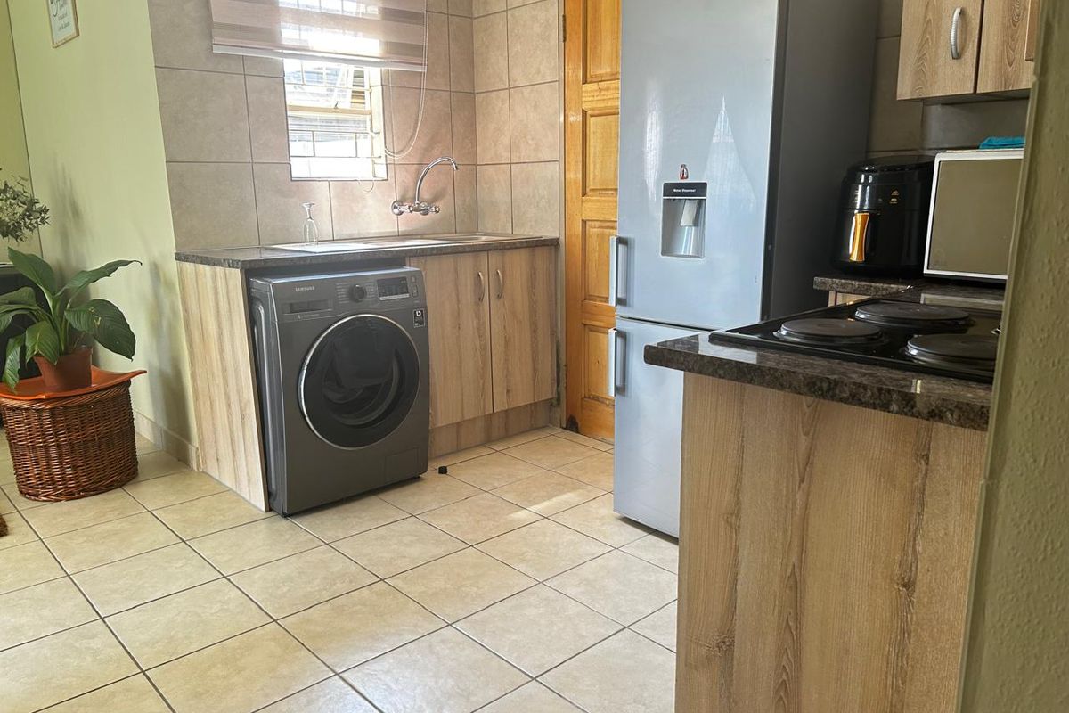 Functional kitchen featuring wood-look cabinetry, granite countertops, tiled splashbacks, and integrated space for laundry appliances.