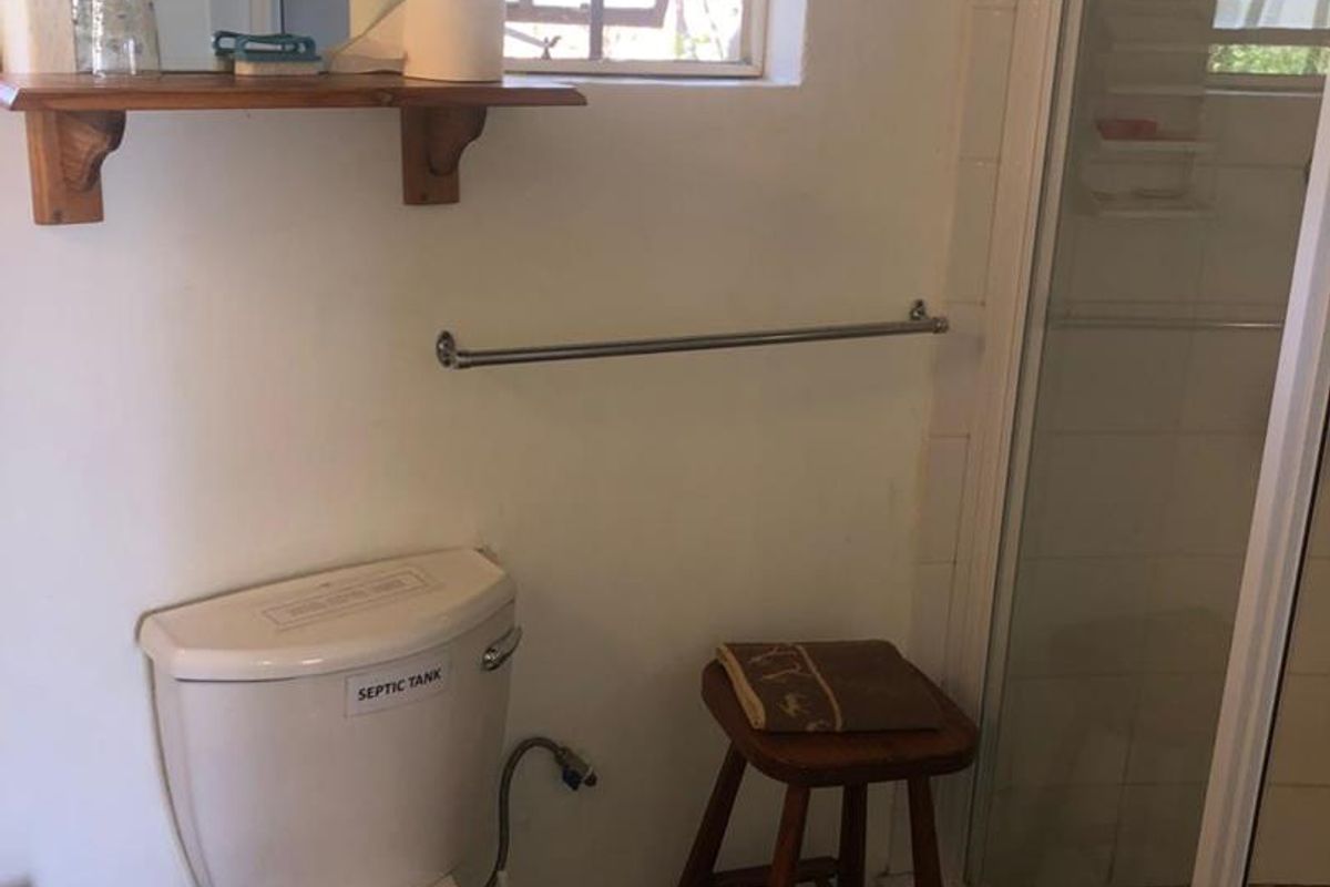 A functional bathroom featuring a toilet, a glass-enclosed shower, and a wall-mounted shelf, requiring cosmetic updates to modernize the space.