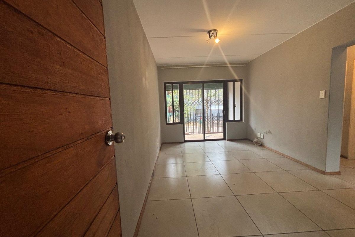 An empty living room featuring tiled flooring, neutral walls, and a sliding glass door with a security gate leading to the exterior.