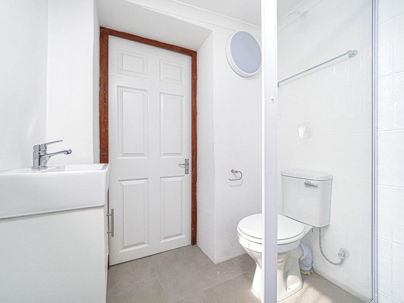 A compact bathroom featuring a vanity basin, toilet, and shower enclosure with white wall tiling and neutral floor tiles.