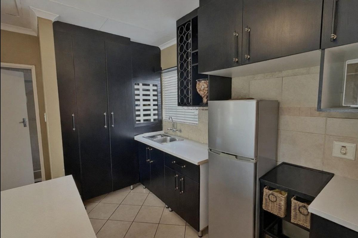 A compact kitchen featuring dark cabinetry, a stainless steel sink, tiled backsplash, and tiled flooring, offering efficient storage and workspace.