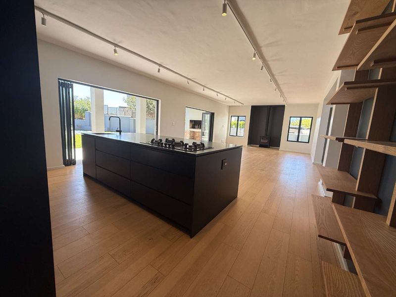 Spacious open-plan living area featuring a modern kitchen island with integrated hob, timber flooring, track lighting, and a sleek wood-burning fireplace.