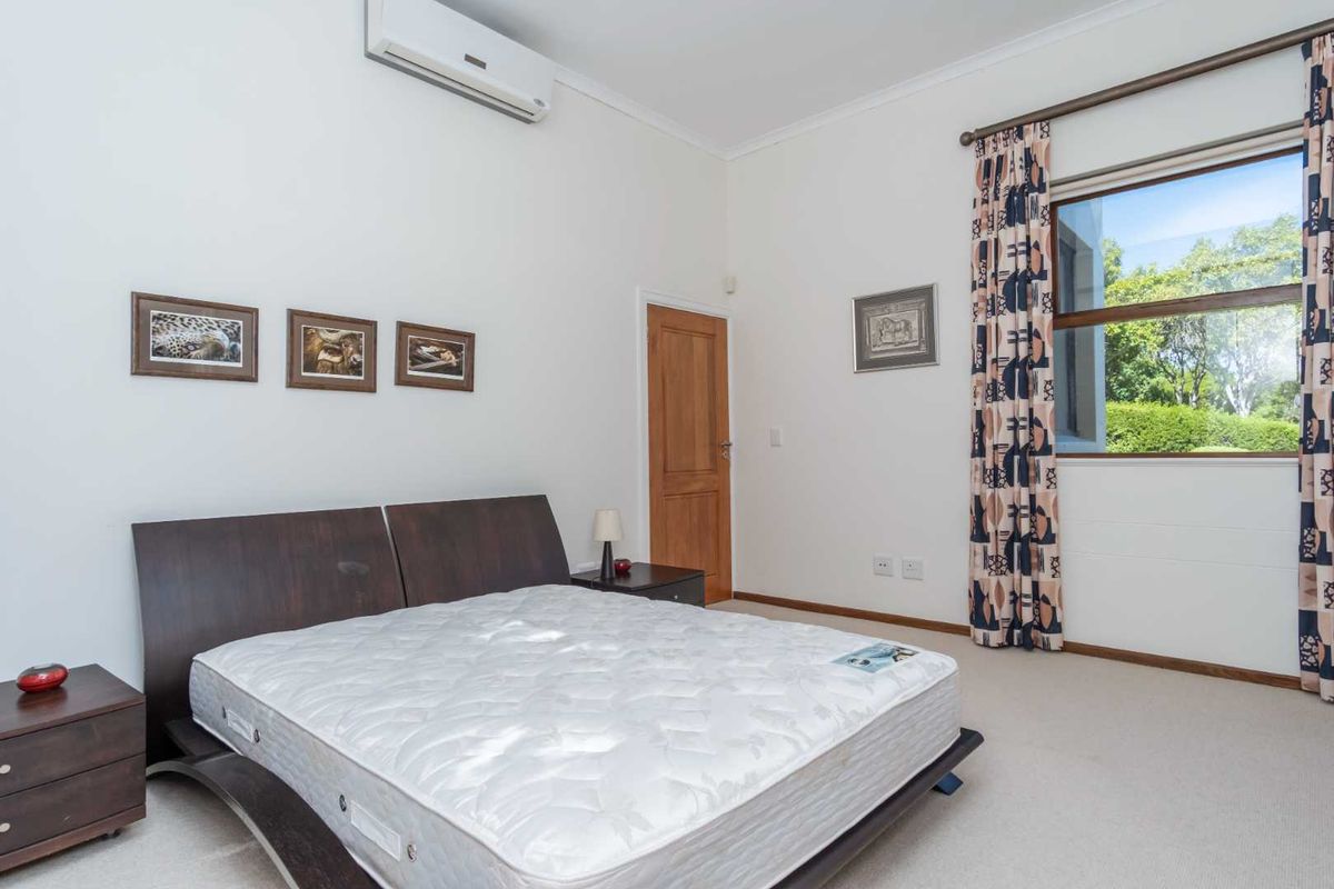 A bedroom featuring carpeted flooring, a wall-mounted air conditioning unit, and a window with garden views.