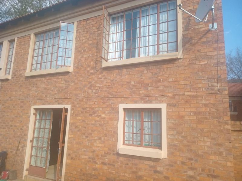 Rear elevation of a face brick townhouse featuring steel-framed windows with security bars and a satellite dish installation.