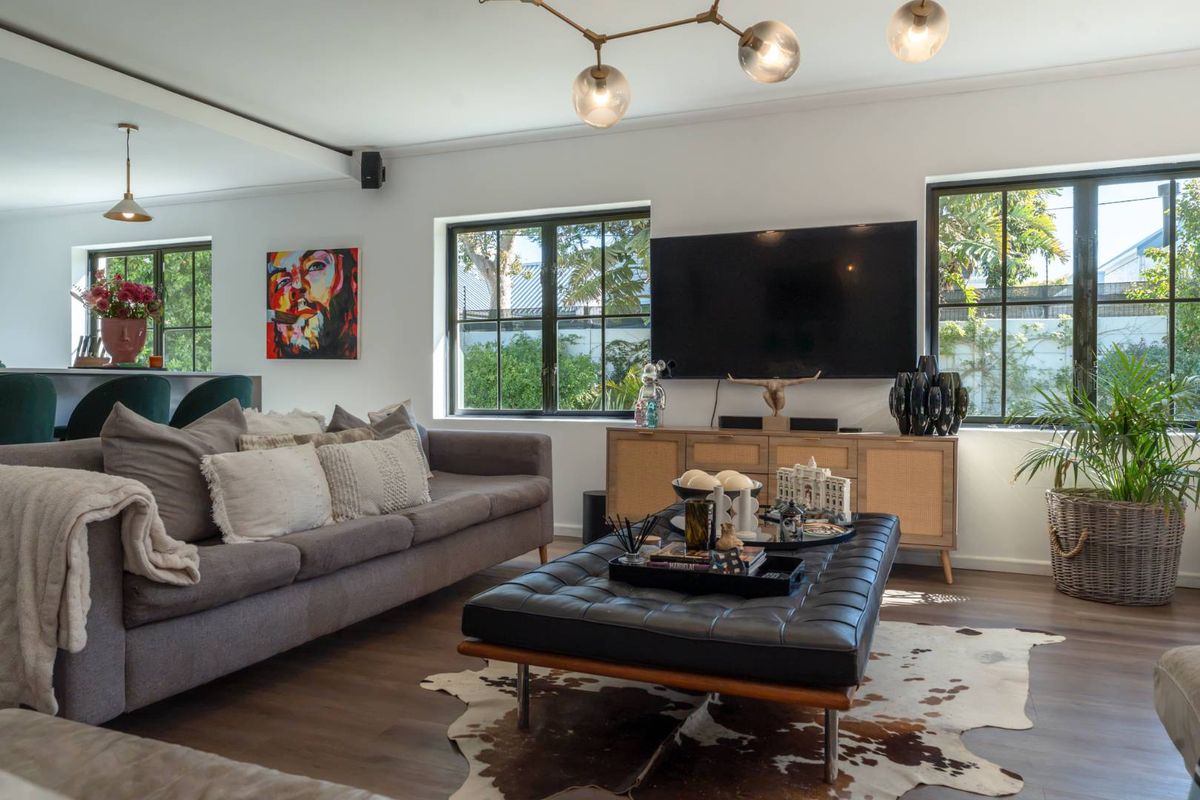 A bright and modern living room featuring dark laminate flooring, large black-framed windows, and contemporary pendant lighting, creating a warm and inviting atmosphere.