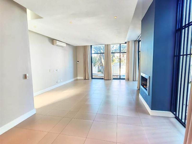 Spacious, light-filled living area featuring large windows, tiled flooring, recessed lighting, a built-in fireplace, and a wall-mounted air conditioning unit.