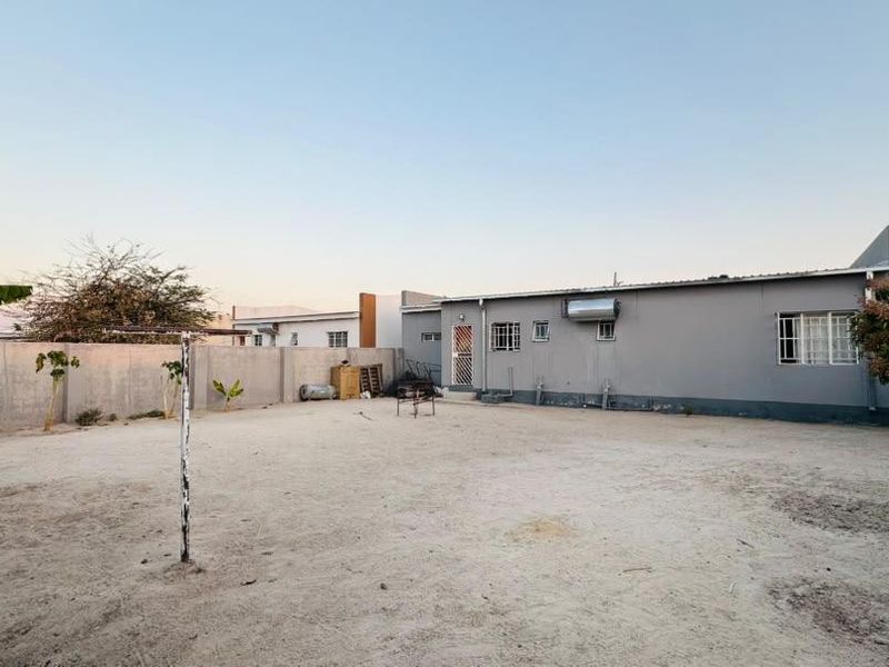 Rear view of the property featuring a large, unlandscaped sandy yard, perimeter wall, and exterior wall-mounted solar geyser.