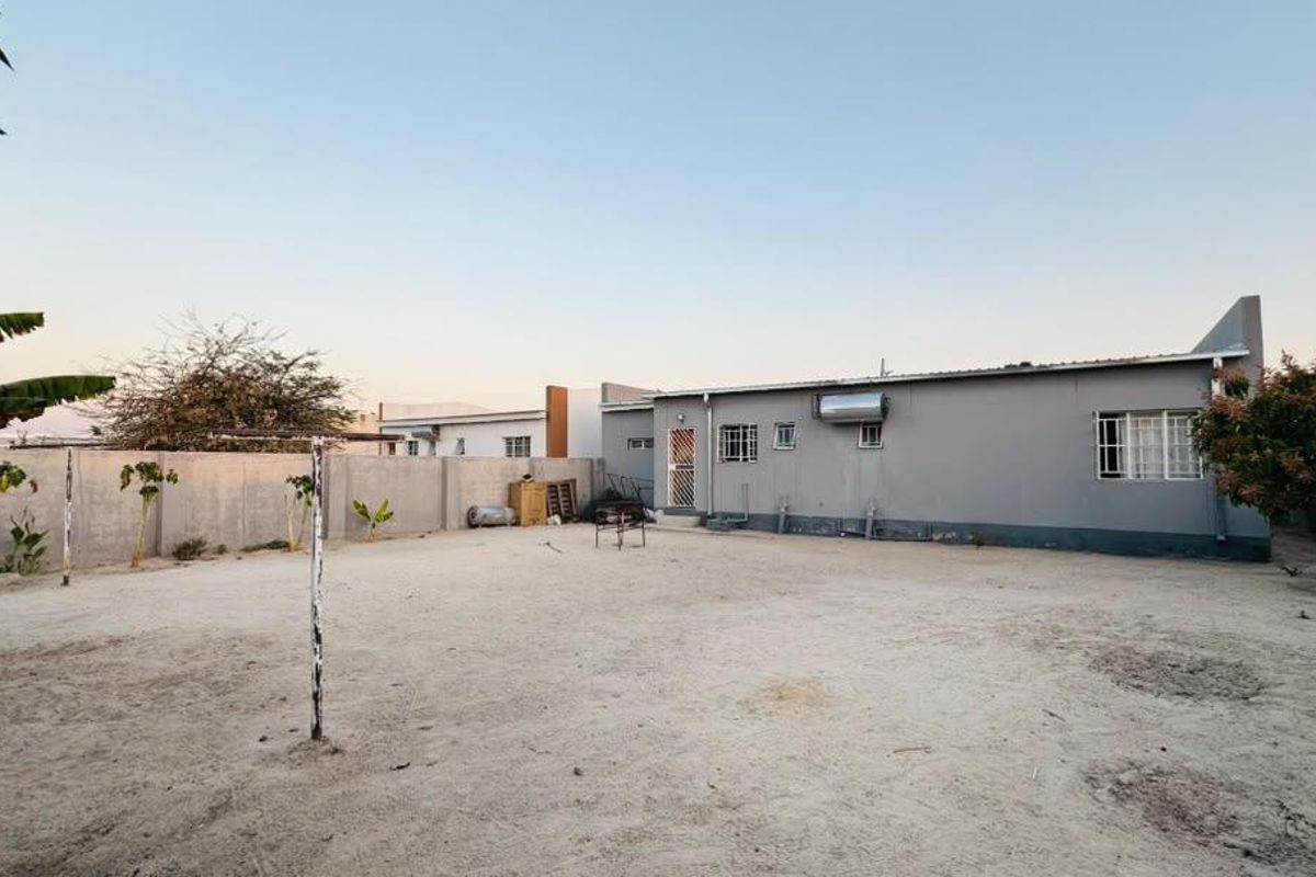 Rear view of the property featuring a large, unlandscaped sandy yard, perimeter wall, and exterior wall-mounted solar geyser.