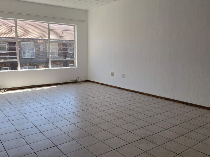 A bright, empty living room featuring neutral tiled flooring, large windows with security bars, and a clean, blank canvas ready for personalization.