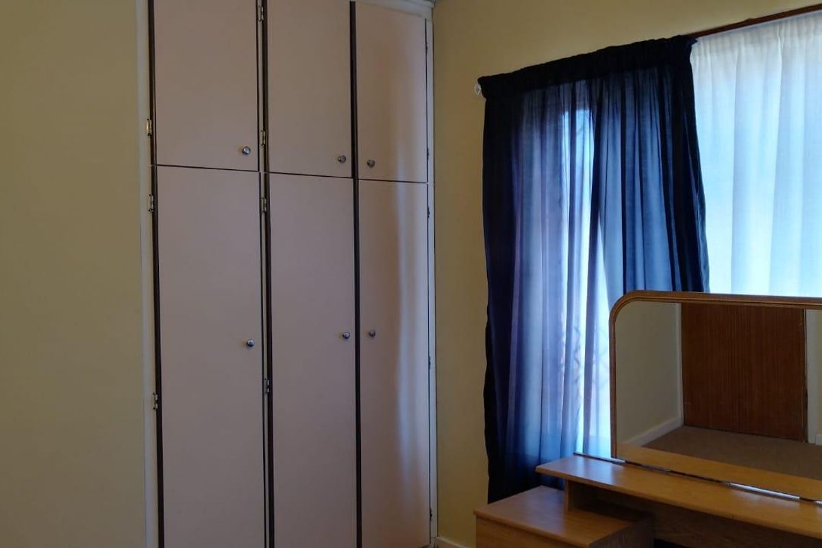 A bedroom featuring built-in floor-to-ceiling cabinetry and a window with curtains.