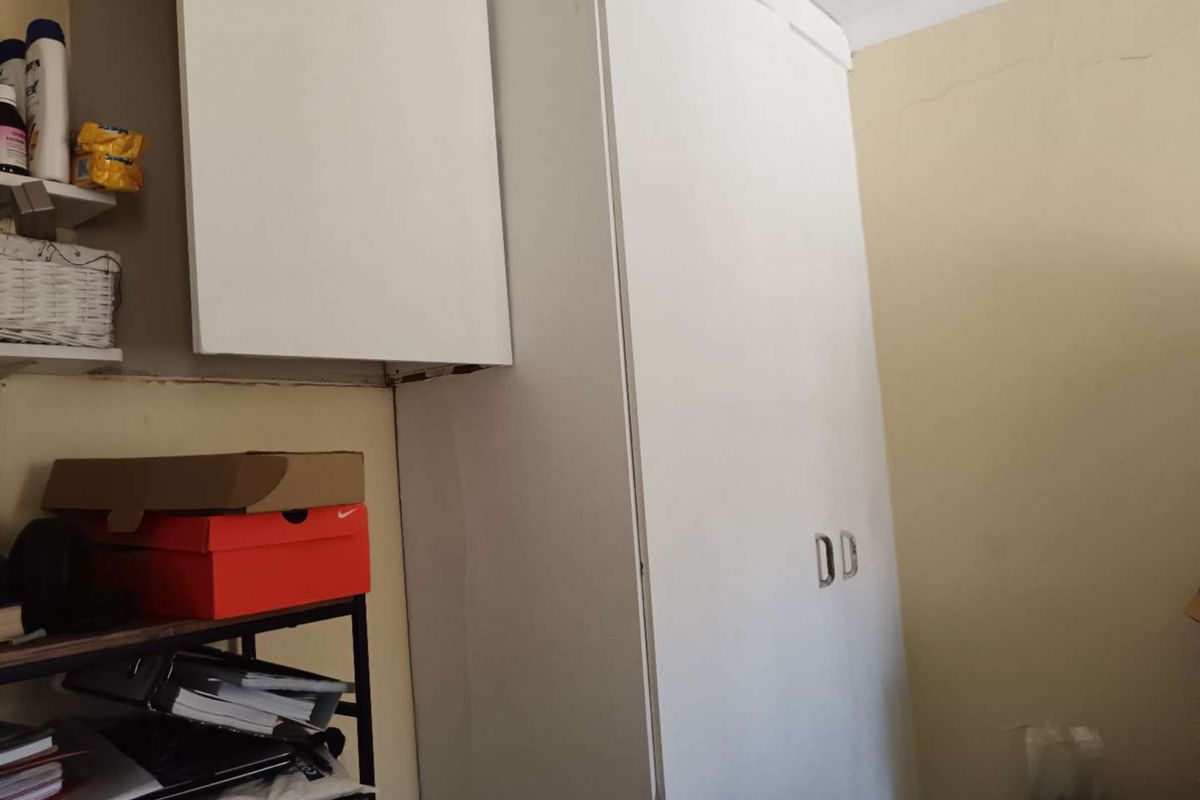 A bedroom interior featuring a white built-in wardrobe with visible wall plaster cracking, requiring minor maintenance and cosmetic updates.
