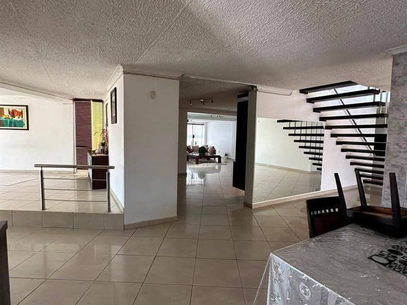 Spacious open-plan living area featuring tiled flooring, a distinctive open-tread staircase with metal balustrade, and a mirrored wall feature.