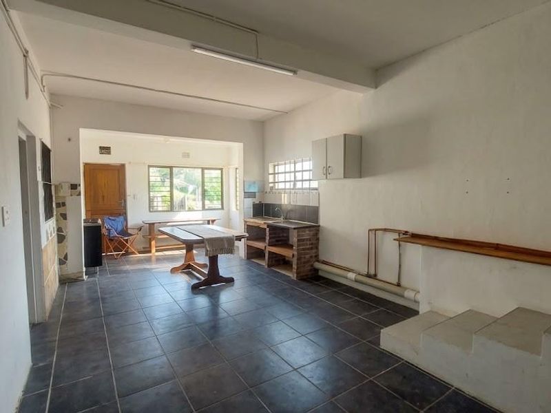 Open-plan living and kitchen area featuring dark tiled flooring, exposed plumbing, and basic built-in cabinetry, offering a blank canvas for renovation.
