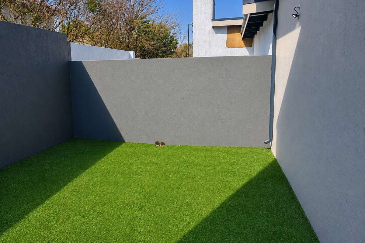 A private rear courtyard area featuring artificial turf, enclosed by high boundary walls with an adjacent building facade.