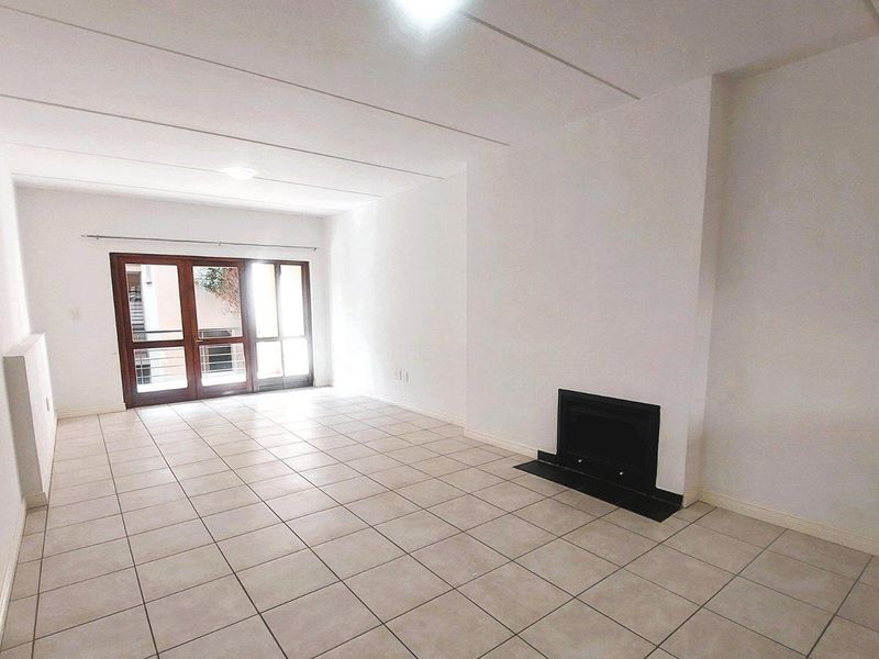 A spacious, empty living room featuring neutral tiled flooring, a built-in fireplace, and large sliding glass doors providing natural light.