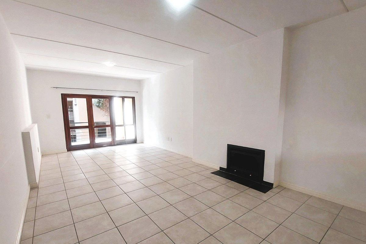 A spacious, empty living room featuring neutral tiled flooring, a built-in fireplace, and large sliding glass doors providing natural light.