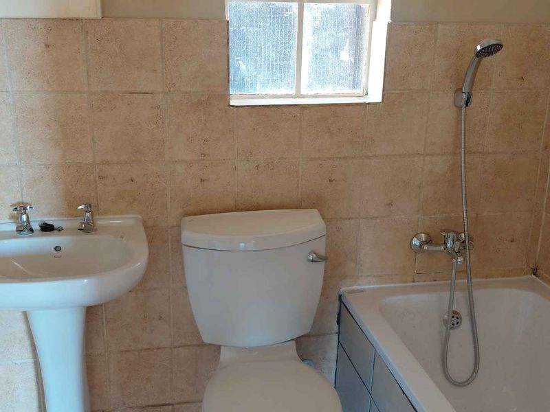 A functional bathroom featuring a pedestal basin, toilet, and bathtub with a handheld shower mixer, finished with neutral wall tiling.