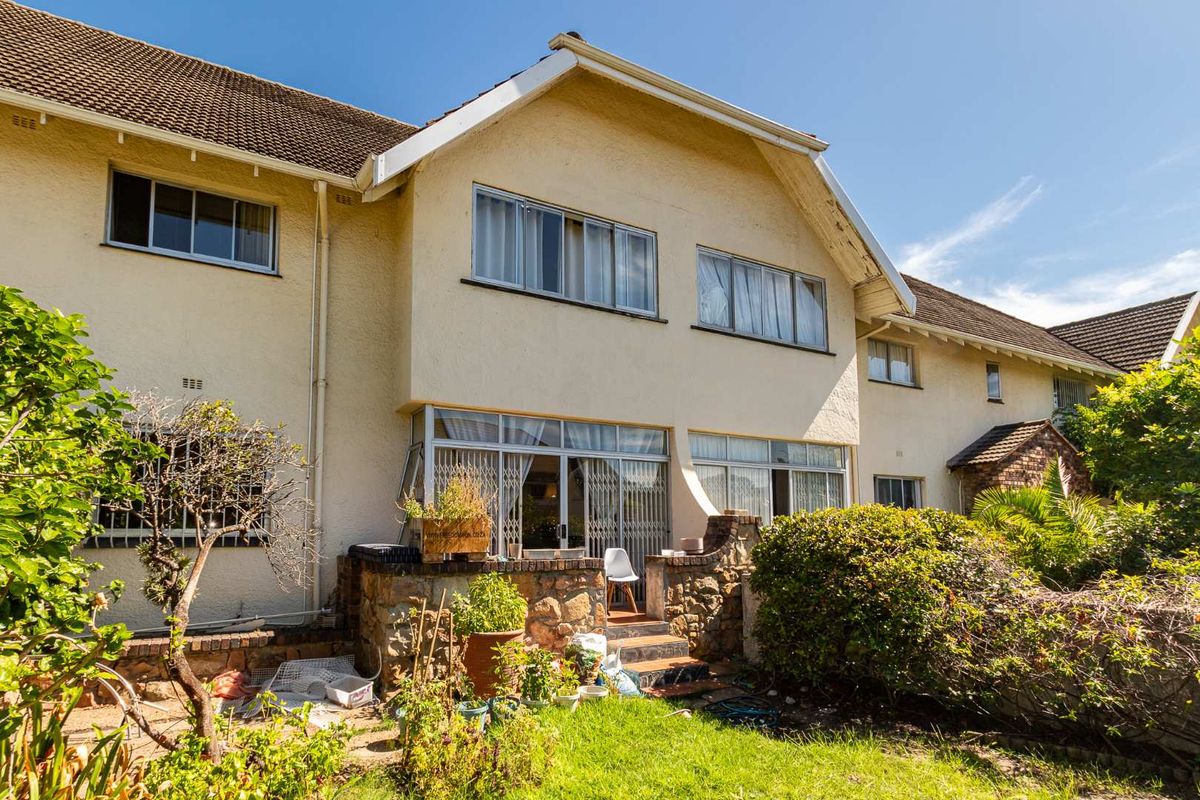 Rear view of the apartment building featuring a paved patio area, stone retaining wall, and established garden space.