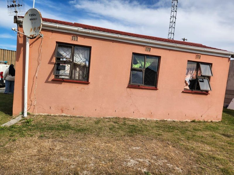 Rear exterior view of a single-story house featuring a tiled roof, aluminium window frames with burglar bars, and a satellite dish installation.